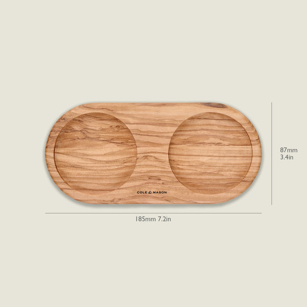 The Cole & Mason Portobello Olive Wood Mill Tray features an oval shape with two circular indentations, ideal for holding salt and pepper mills. It measures 185mm x 87mm and is shown against a plain background.