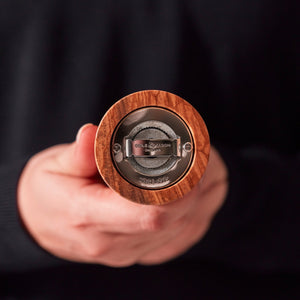#salt&pepperset A person holds a Cole & Mason Portobello Olive Wood Salt & Pepper Mill toward the camera, highlighting its precision grinding mechanism and branded base.