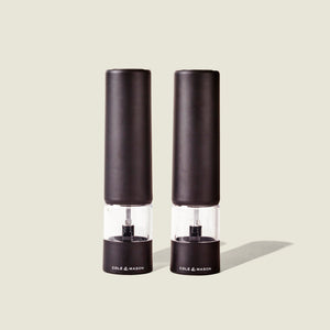 Two sleek, matt black electric grinders labeled Cole & Mason Brixton Electric Mill stand side by side against a plain, light background, each featuring a durable ceramic grinder for smooth and precise seasoning with convenient one-hand operation.