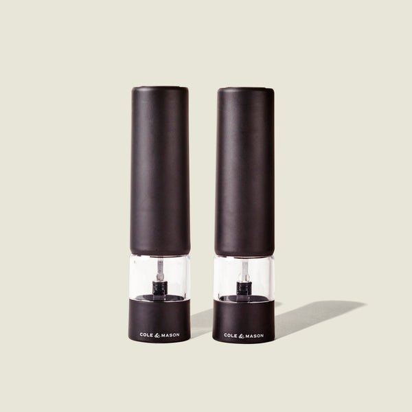 Two sleek, matt black electric grinders labeled Cole & Mason Brixton Electric Mill stand side by side against a plain, light background, each featuring a durable ceramic grinder for smooth and precise seasoning with convenient one-hand operation.