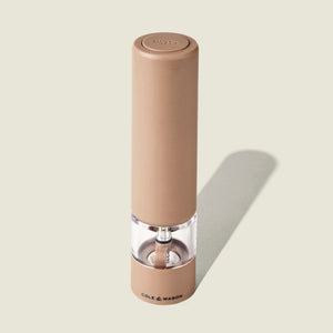 A tan, cylindrical Cole & Mason Brixton Electric Mill Stone GS pepper grinder with a transparent mid-section displaying peppercorns inside, featuring adjustable grind settings for customized seasoning, stands upright on a light background with the brand name visible at its base.