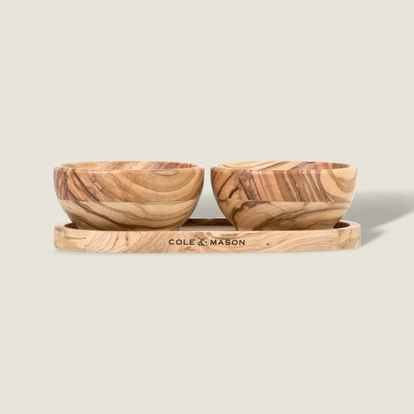 The Cole & Mason Portobello Olive Wood Pinch Pot Set features two small pots with unique grain patterns on a matching tray engraved with the brand name. The set is displayed against a plain, light beige background.