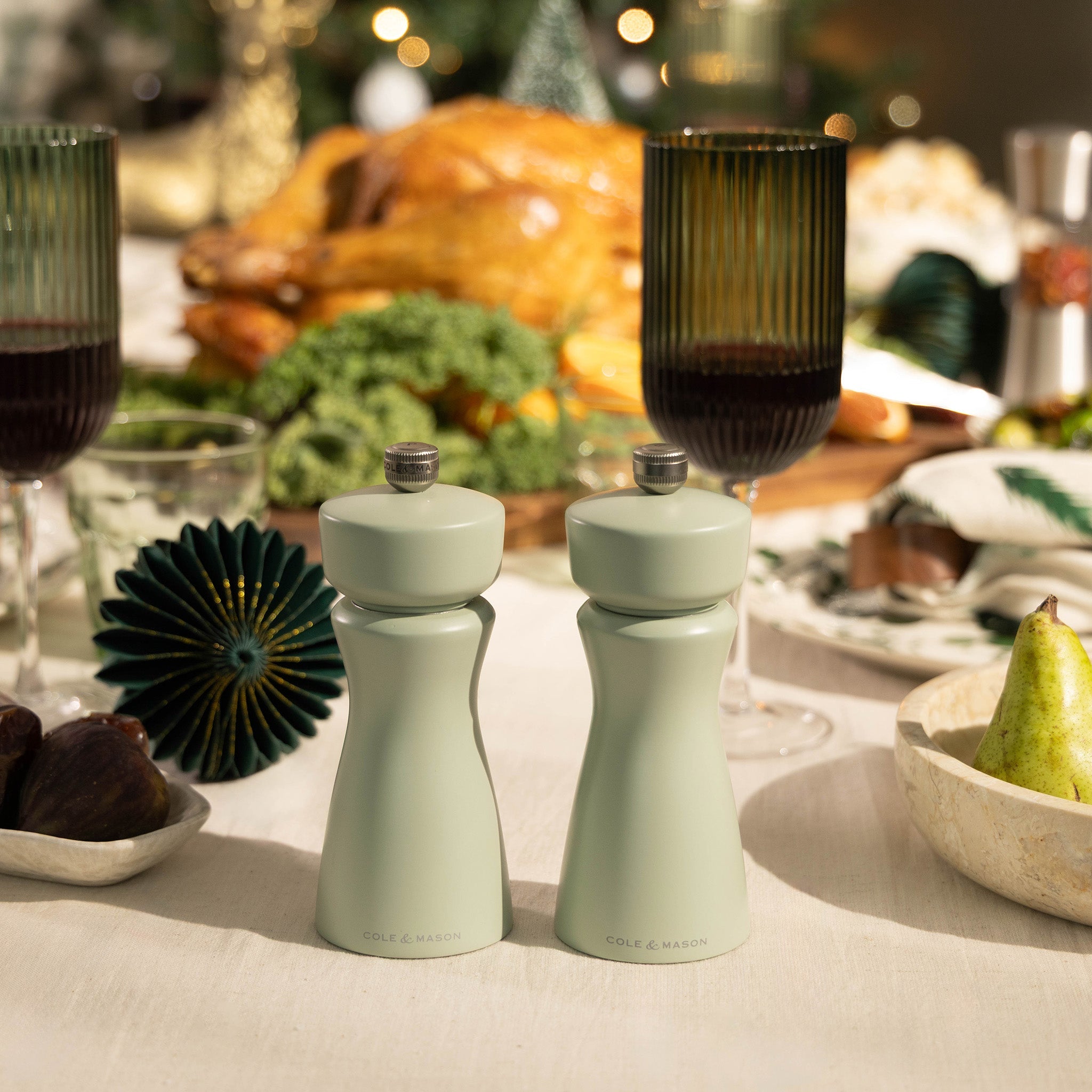The Cole & Mason Kenton Mills in Sage Christmas Gift Hamper features elegant salt and pepper grinders on a festive table—an ideal gift for holiday gatherings.