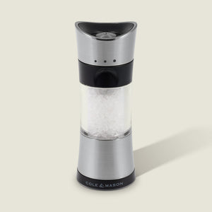 A Cole & Mason Horsham Salt & Pepper Mill in stainless steel and clear acrylic, filled with coarse salt, stands upright on a light background with a right-side shadow and the COLE & MASON logo at its base.
