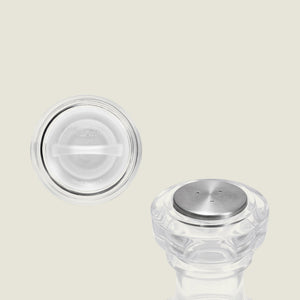 Two clear, round Cole & Mason Acrylic Salt Shaker & Pepper Mill Set (104 mm) pieces with metal tops are displayed on a light background; one stands upright while the other reveals its flat underside with embossed text. Ideal for pairing with your favorite adjustable grinder, this elegant set adds a classic touch to any table setting.