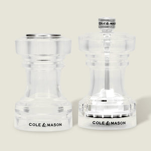 A pair of Cole & Mason Acrylic Salt Shaker & Pepper Mill Set (104 mm) are displayed side by side on a light background. Both mills feature clear acrylic bodies with the Cole & Mason logo at the base, flat and round tops, and visible grinding mechanisms that allow you to adjust the coarseness of your spices for a customizable seasoning experience.