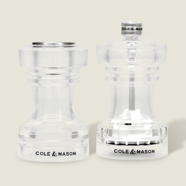 A pair of Cole & Mason Acrylic Salt Shaker & Pepper Mill Set (104 mm) are displayed side by side on a light background. Both mills feature clear acrylic bodies with the Cole & Mason logo at the base, flat and round tops, and visible grinding mechanisms that allow you to adjust the coarseness of your spices for a customizable seasoning experience.