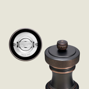 A close-up of the Cole & Mason Hoxton Salt and Pepper Mill, featuring antique bronze and copper accents, highlights the grinding system and the “P” label on top.
