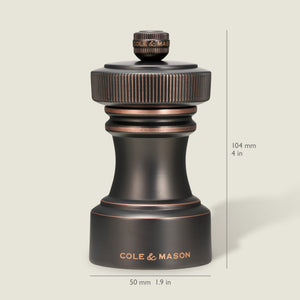 A dark metallic pepper grinder from the Cole & Mason Hoxton Salt and Pepper Mill Set in an antique bronze finish is shown upright against a light background, labeled with the brand name. The mill measures 104 mm (4 in) tall and 50 mm (1.9 in) wide, and features a precise grinding system for consistent seasoning—perfect for pairing with any salt or pepper mill set.