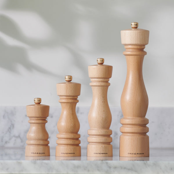 Cole & Mason London beech wood mills in four sizes lined up on a marble kitchen counter