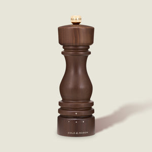 A London Walnut Salt or Pepper Mill from Cole & Mason, featuring dark walnut wood with a rounded top and base, stands upright on a light beige background.