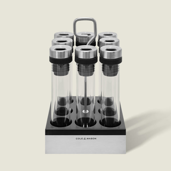 The Cole & Mason Shadwell Countertop Spice Storage features eight airtight glass jars in a stainless steel square holder with a metal handle for easy countertop organization.